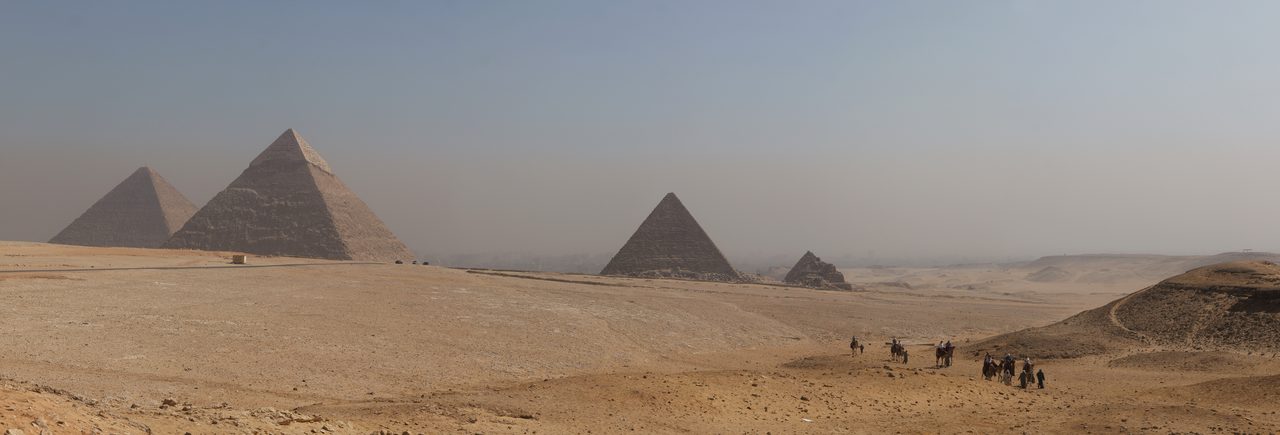 A wide panorama of the pyramids of the Giza plateau in Egypt, lined up across the desert horizon.