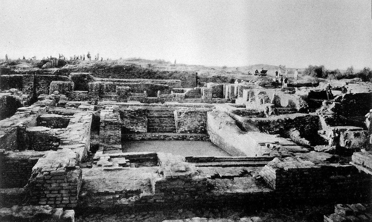 A black and white photograph of the excavated Great Bath at Mohenjo-daro, a large rectangular brick basin set within brick walls