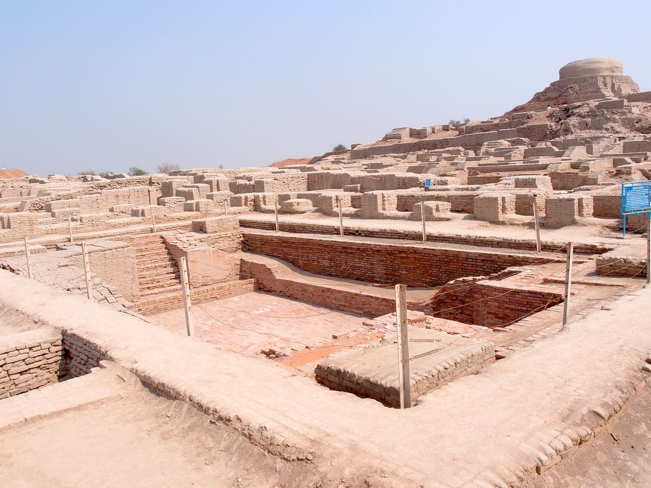 The excavated brick ruins of Mohenjo-daro under a clear sky, streets and walls laid out across the site