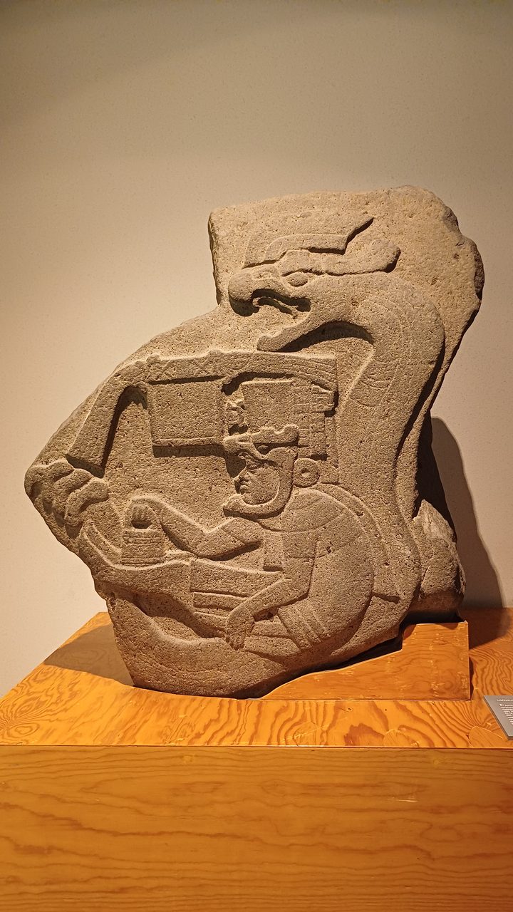 Olmec Monument 19 from La Venta, a seated figure entwined with a serpent and carrying a small bag