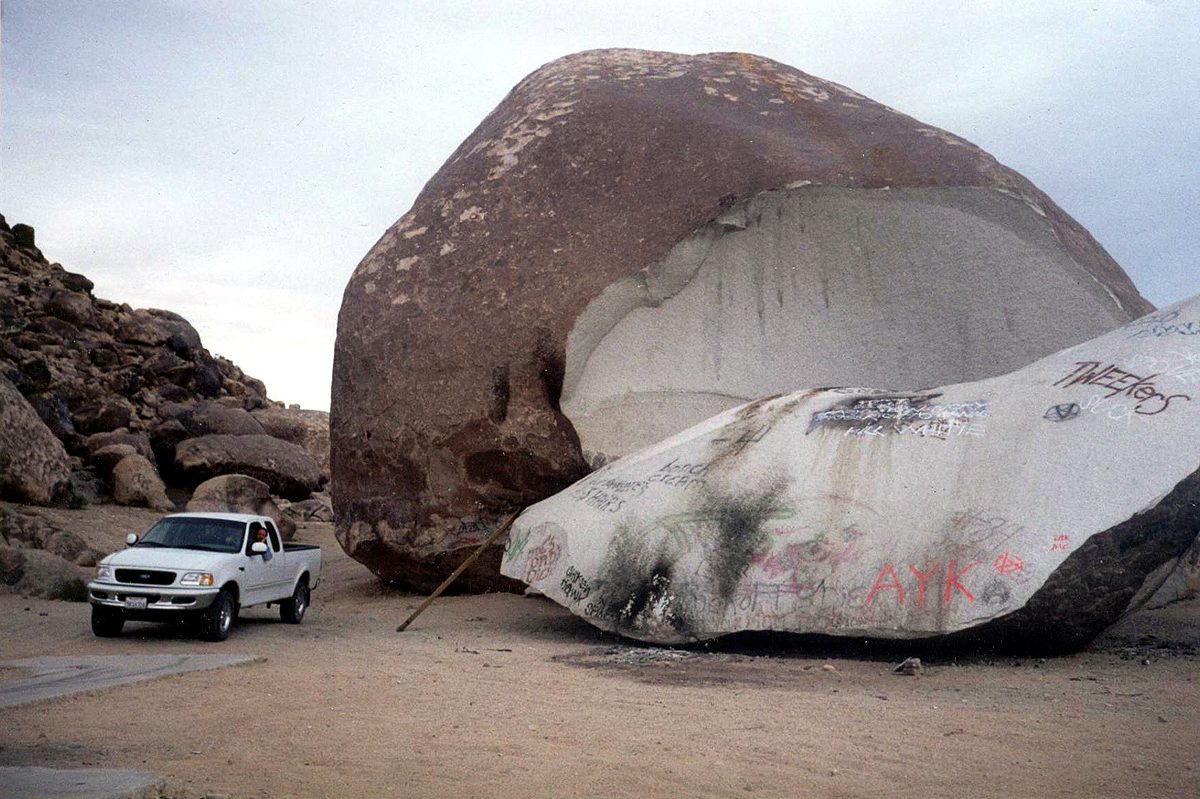 A pickup truck parked beside Giant Rock near Landers, California, showing the boulder's true scale