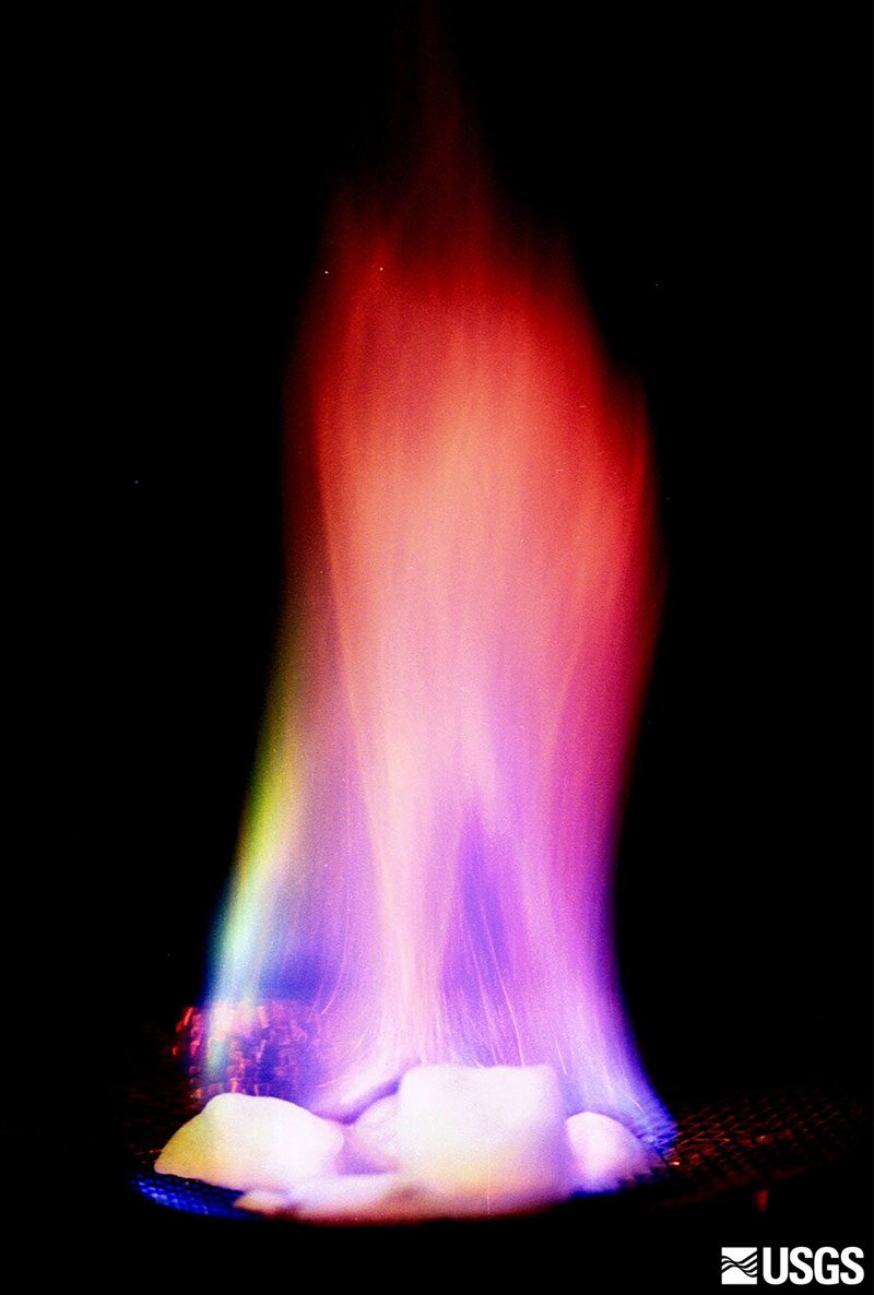 A lump of methane hydrate burning with a yellow flame while sitting on a gloved hand, a U.S. Geological Survey demonstration of the ice that burns