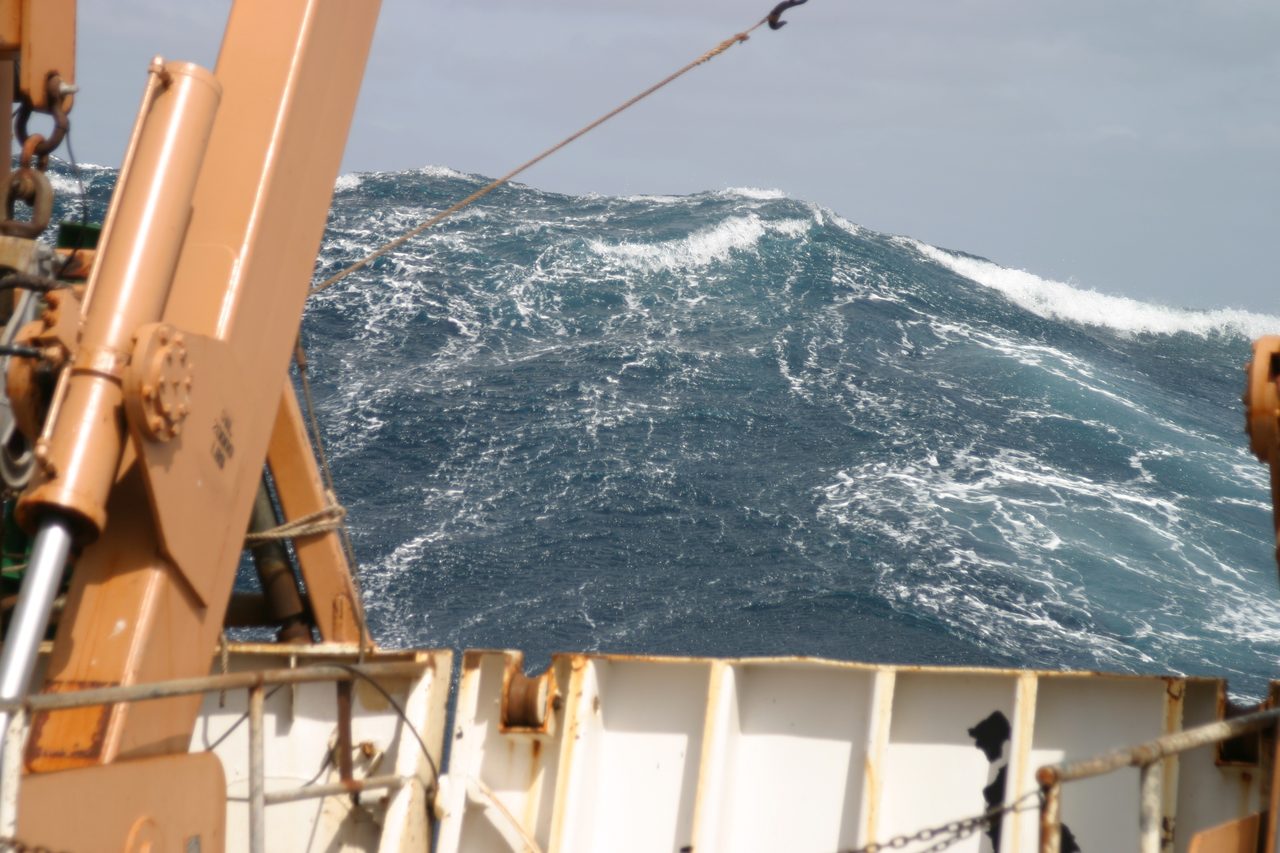 A large wave rising astern of a NOAA research ship on a grey, heaving Atlantic Ocean