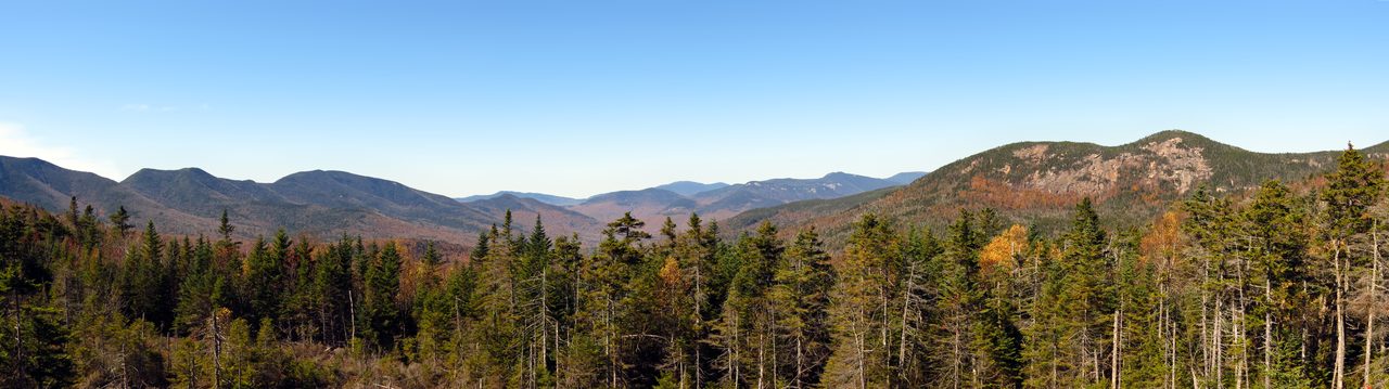 A wide daytime vista of forested mountain ridges under a partly cloudy sky in the White Mountain National Forest, New Hampshire.