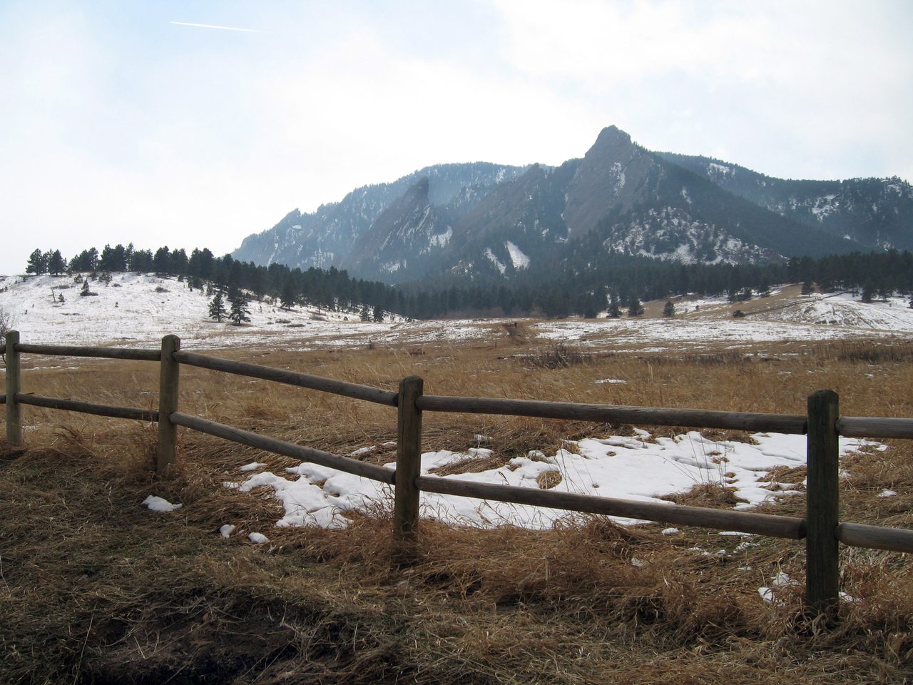 Not Bosnia: a split-rail wooden fence and a snowy winter meadow in the foreground, with the tilted triangular sandstone slabs of the Flatirons standing along the ridge behind, at Chautauqua Park in Boulder, Colorado