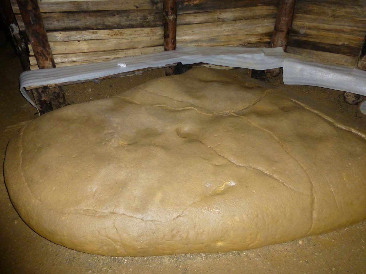A large smooth rounded stone lying on the sandy floor of a chamber in the Ravne tunnel network near Visoko, beneath a wall of modern sawn timber shoring and white foam matting