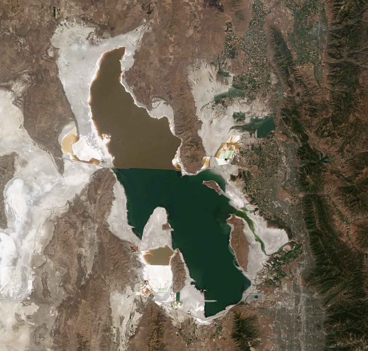 A satellite view of the Great Salt Lake showing a sharp color contrast between its two arms across a causeway.