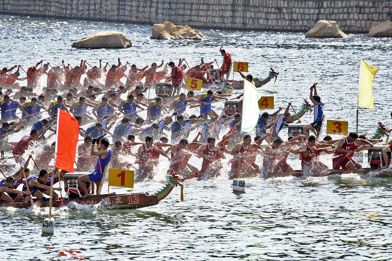 Dragon boat teams racing, each long boat carrying a carved dragon head at the prow and a drummer at the bow