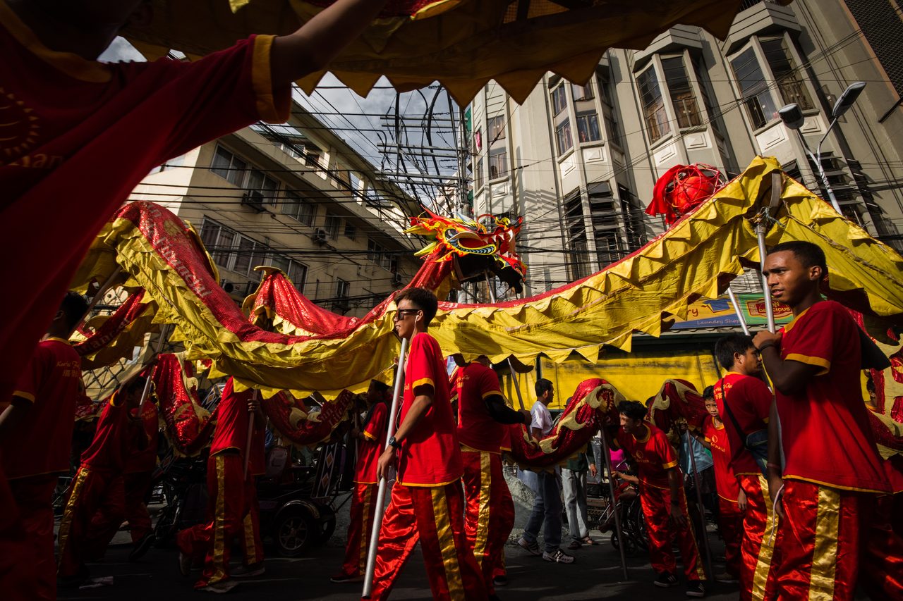 A dragon dance in the street in Binondo, Manila, performers in red and gold carrying the dragon on poles