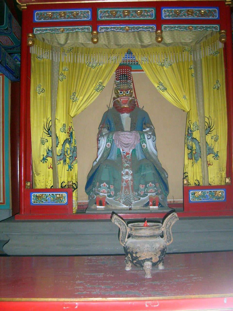 A painted statue of a Dragon King enshrined in a temple niche, with an incense censer set before it