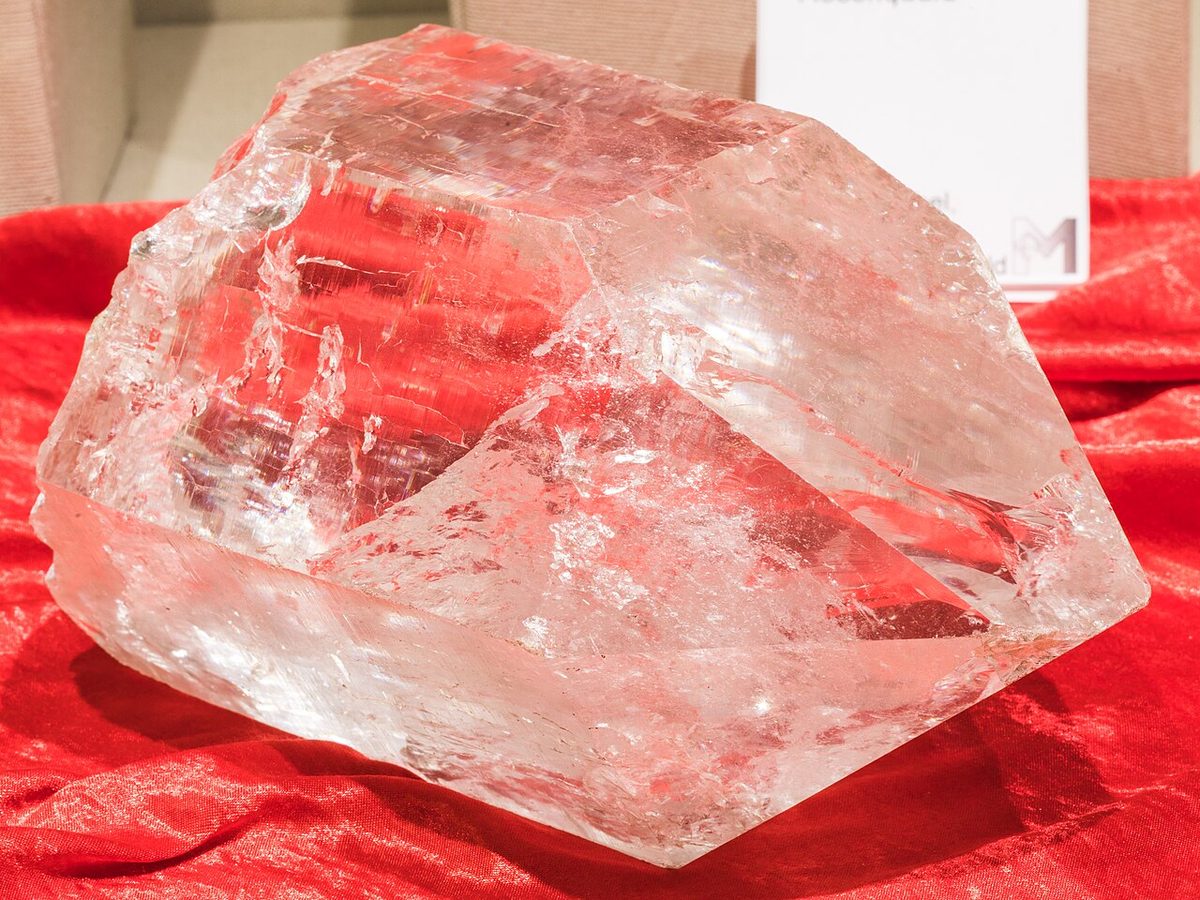 A single large block of natural clear quartz crystal on a red display cloth