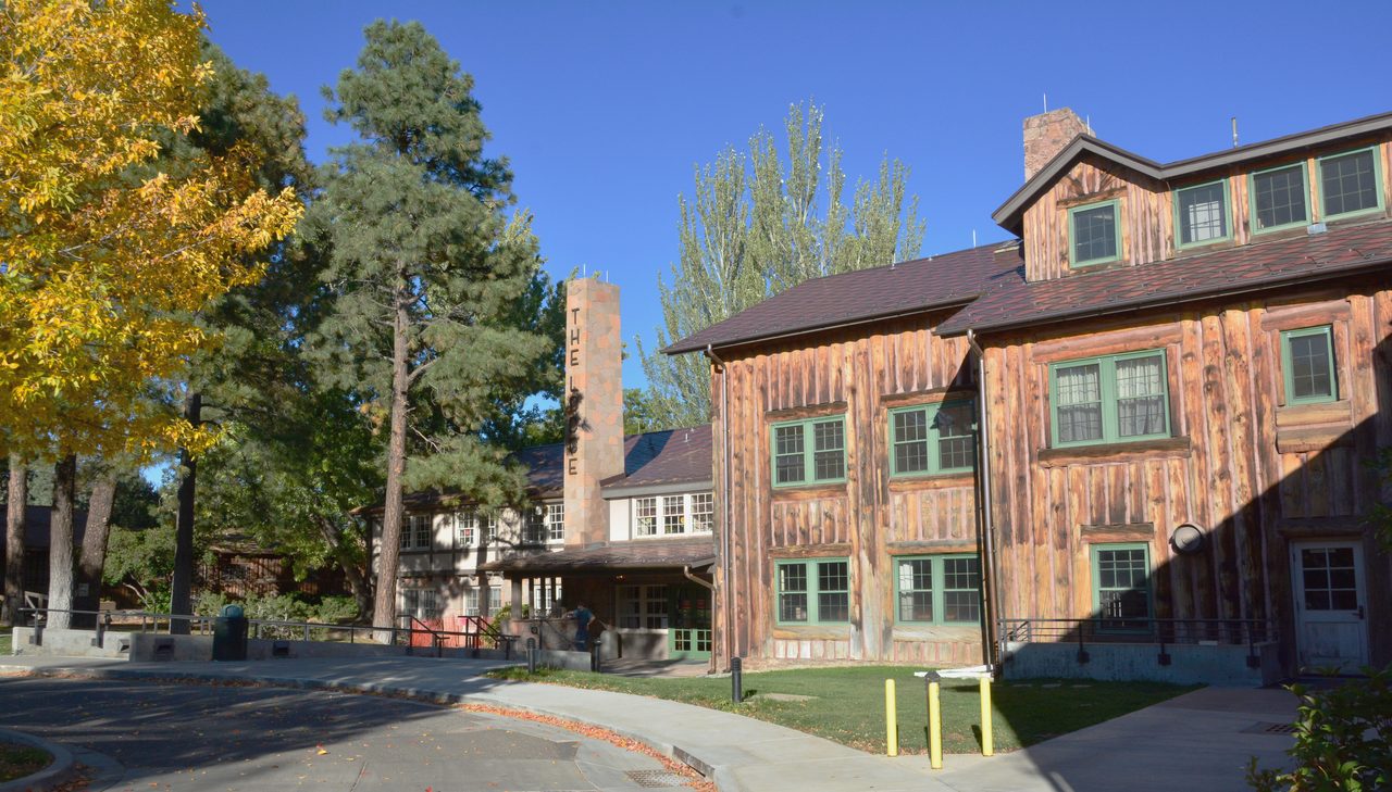 Fuller Lodge in Los Alamos, a long building of massive vertical log slabs with a stone chimney, under a blue sky.
