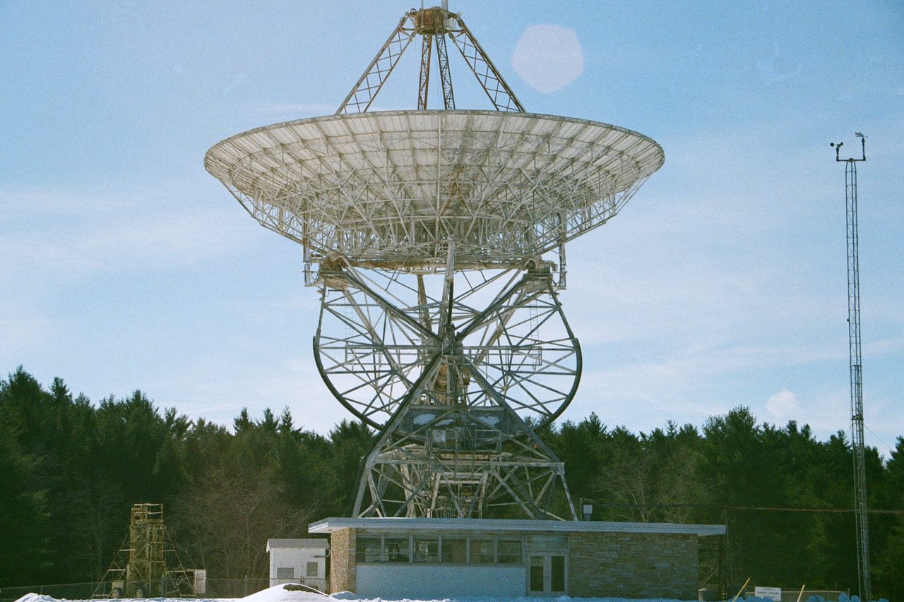 The 85 foot Howard E. Tatel radio telescope at Green Bank, its open lattice dish standing above a low control building in deep snow.