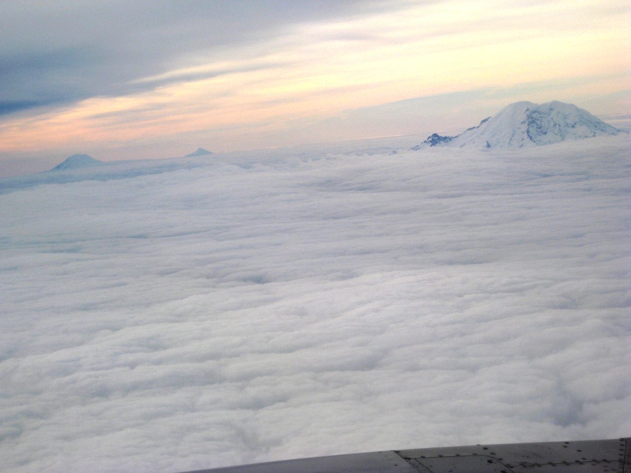 Three Cascade summits breaking above an unbroken deck of cloud, seen from the air in low sun