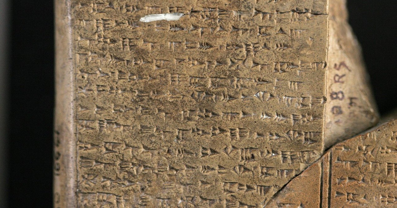 A close view of a clay tablet densely covered in cuneiform wedges, with an inked excavation number on its edge