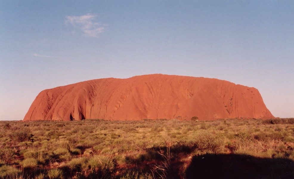 The great sandstone monolith of Uluru rising from a flat desert plain in central Australia