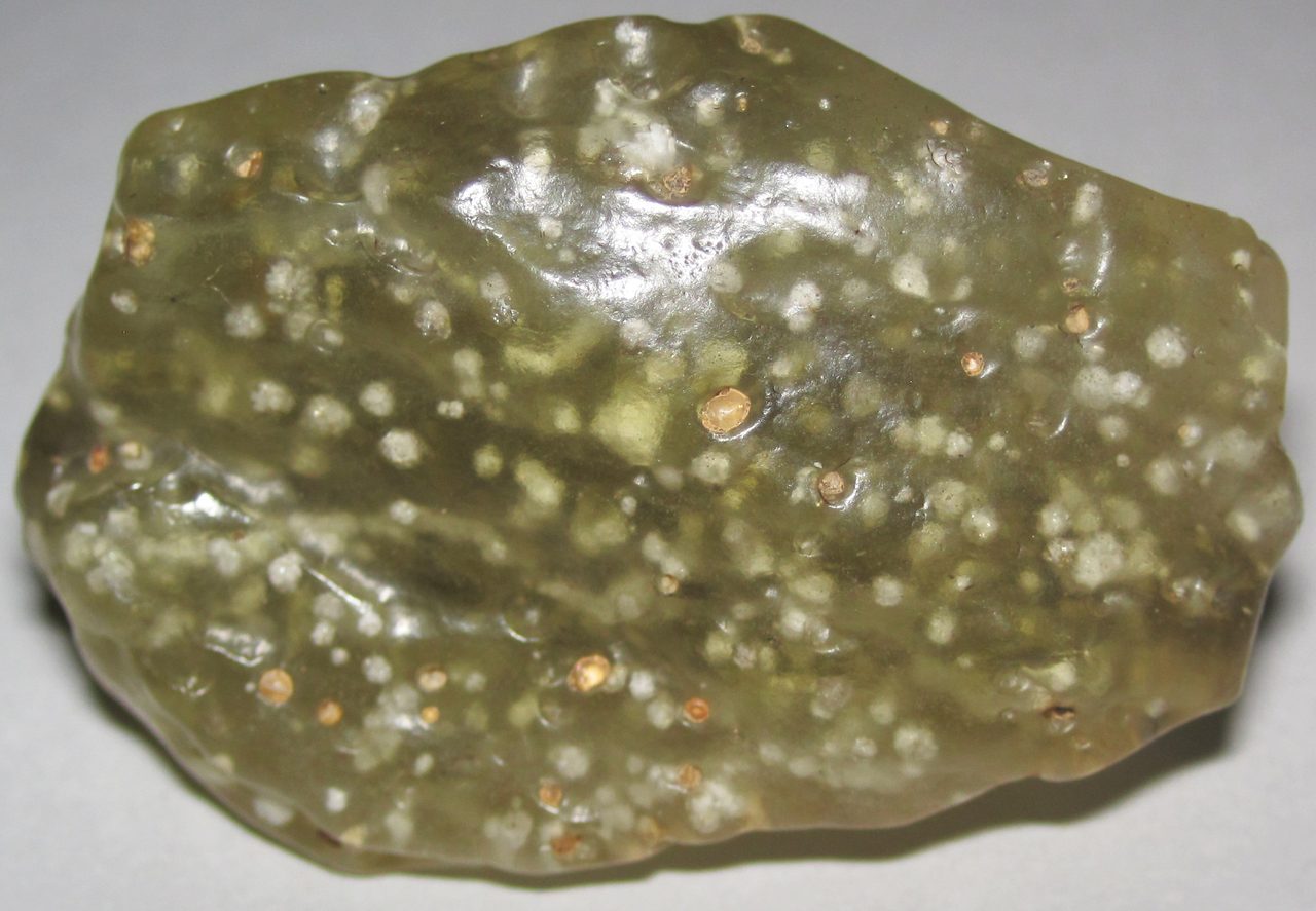 A macro photograph of a Libyan Desert Glass specimen, a pale yellow translucent natural glass with small rounded inclusions scattered across its surface.