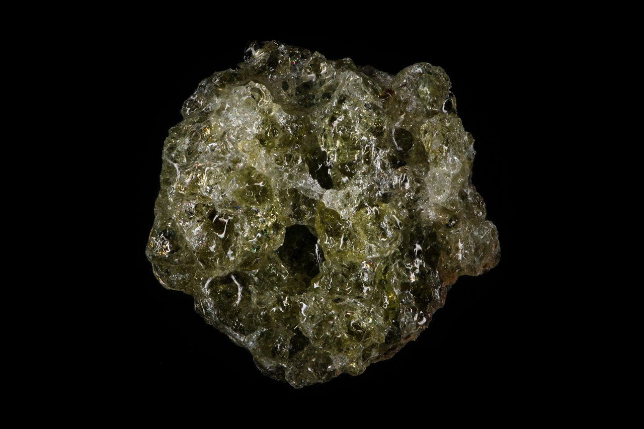 A macro photograph of trinitite, a thin grayish-green glassy crust formed on the ground by the 1945 Trinity nuclear test.