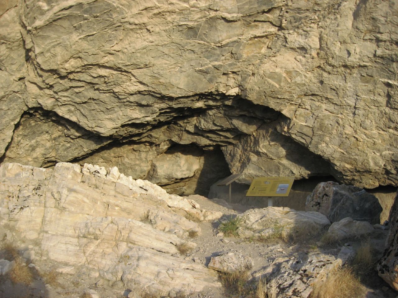 The entrance to Lovelock Cave near Lovelock, Nevada, seen from outside, with a yellow interpretive panel on a post standing in front of the opening