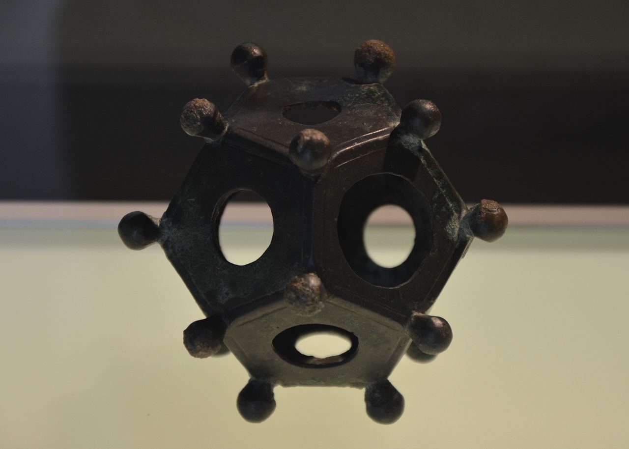 A bronze Roman dodecahedron from the Gallo-Roman Museum of Tongeren, Belgium, showing its pentagonal faces, varying circular holes, and knobbed vertices