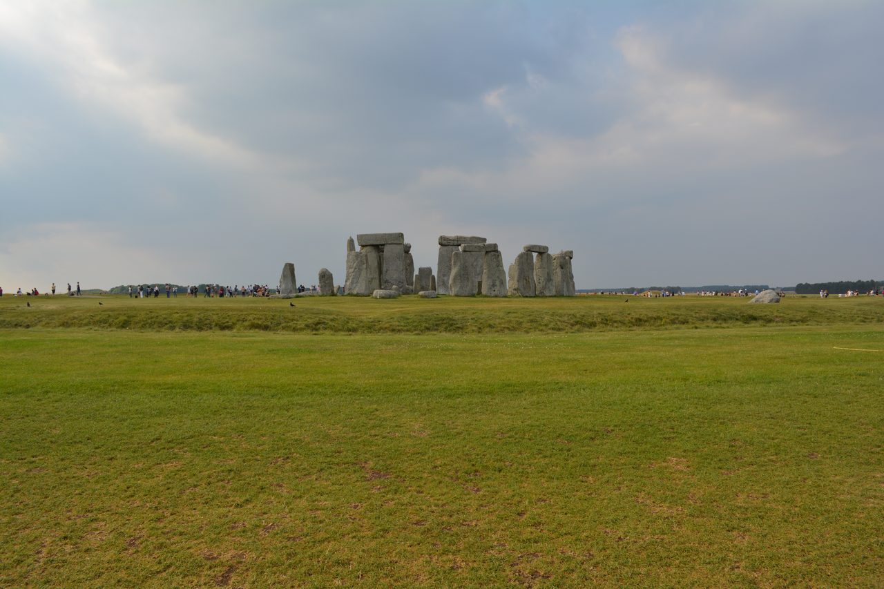 A wide ground-level view of Stonehenge from the southeast showing the sarsen circle and the trilithon horseshoe under an overcast sky