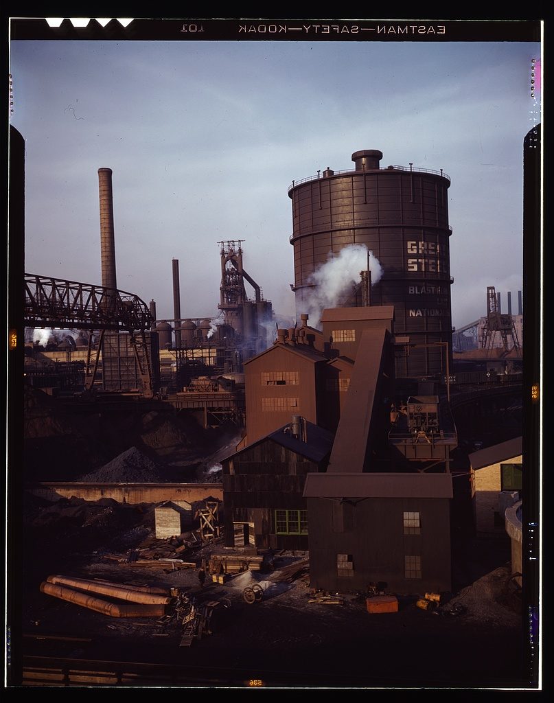 A 1942 black-and-white photograph of a Great Lakes Steel Corporation blast-furnace facility on the Detroit riverfront, with tall industrial structures and a gas storage tank
