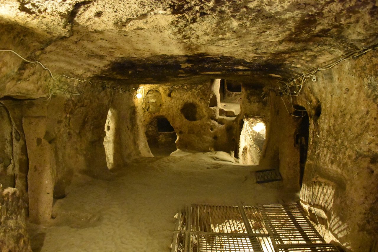 A narrow rock-cut passage descending into a multi-level underground city carved from soft volcanic tuff