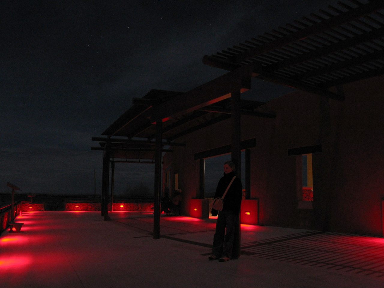 A nighttime long-exposure photograph of the Marfa Lights viewing platform, a low masonry structure beside a Texas highway under a dark sky